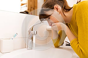 Young vomiting woman near sink in bathroom