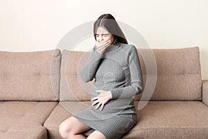 Young vomiting woman sitting on sofa and suffering with nausea. Pregnancy expectation concept, copy space