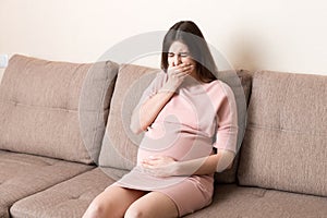 Young vomiting woman sitting on sofa and suffering with nausea. Pregnancy expectation concept, copy space