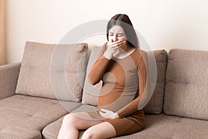 Young vomiting woman sitting on sofa and suffering with nausea. Pregnancy expectation concept, copy space photo