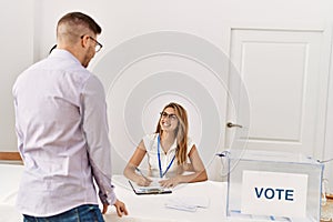 Young voter man standing by electoral table talking with political party worker at vote center