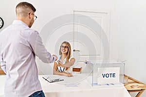 Young voter man standing by voting table giving vote to political party worker at electoral center