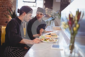 Young wait staff discussing over clipboard and food while sitting at counter