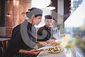 Young wait staff discussing over food with digital tablet and clipboard at counter