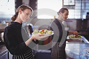 Young wait staff holding fresh salad plates while standing in commercial kitchen