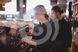 Young wait staff using espresso maker at coffee shop