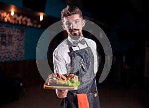 Young waiter helpfully serves dish on a black background.