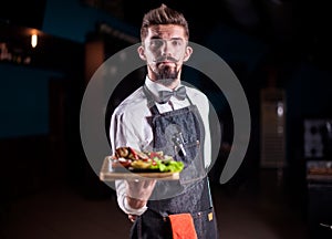 Young waiter helpfully serves dish in the restaurant.