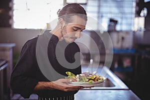 Young waiter holding fresh salad plate in commercial kitchen