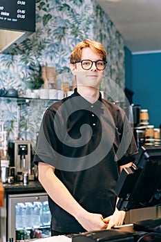 Young waiter serving customer at cash point in cafe. Man working with POS terminal. Cashier, barista checking for