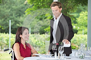 Young waiter serving mature disabled woman at restaurant