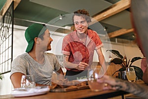 Young waiter talking with a group of smiling bistro customers