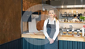 Young waitress wearing apron posing in restaurant. Portrait of a young woman on her first day job in a coffee shop. Smiling young