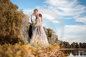 A young wedding couple in love on the edge of a cliff against the backdrop of the river and the sky. A woman in a beautiful gray