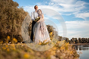 A young wedding couple in love on the edge of a cliff against the backdrop of the river and the sky. A woman in a beautiful gray