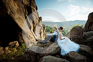 Young wedding couple is sitting back-to-back on the rock. Magnificent landscape view.