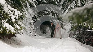Young wedding couple walking, smiling and talking holding hands in snowy forest during snowfall. Winter wedding