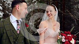 Young wedding couple walking, smiling and talking holding hands in snowy forest during snowfall. Winter wedding