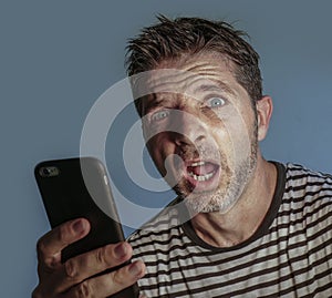 Young weird and crazy mobile phone addict man using cell compulsively with weird and freak face expression in internet social