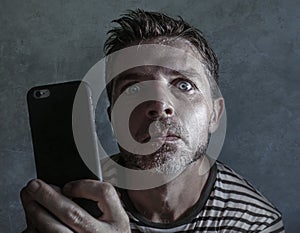 Young weird and crazy mobile phone addict man using cell compulsively with weird and freak face expression in internet social