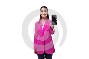 young well-groomed smiling brunette successful boss woman dressed in a pink jacket shows a smartphone with a mockup