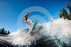 Young wet woman energetically balancing on wave on wakesurf board