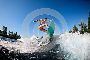 Young wet woman energetically balancing on wave on wakesurf board