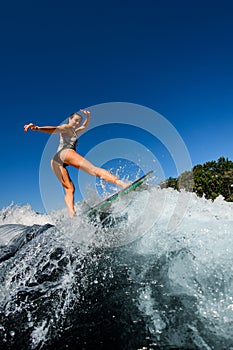 Young wet woman energetically rides the wave on wakesurf board