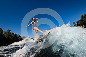Young wet woman confidently stands on the wakesurf board and rides the wave photo