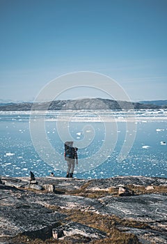 Young white caucasian man with backpack on a hiking trip in Greenland overlooking Atlantic ocean with icebergs. Arctic