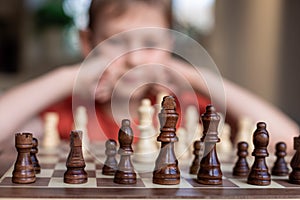 Young white child playing a game of chess on large chess board. Chess board on table in front of school boy thinking of next move