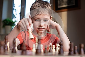 Young white child playing a game of chess on large chess board. Chess board on table in front of school boy thinking of next move