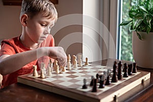 Young white child playing a game of chess on large chess board. Chess board on table in front of school boy thinking of next move