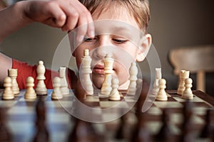 Young white child playing a game of chess on large chess board. Chess board on table in front of school boy thinking of next move