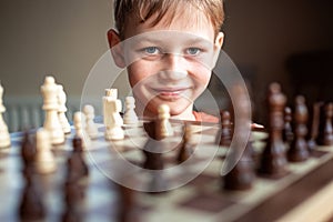 Young white child playing a game of chess on large chess board. Chess board on table in front of school boy thinking of next move