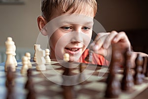 Young white child playing a game of chess on large chess board. Chess board on table in front of school boy thinking of next move