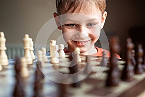 Young white child playing a game of chess on large chess board. Chess board on table in front of school boy thinking of next move