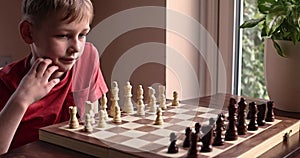 Young white child playing a game of chess on large chess board. Chess board on table in front of school boy thinking of next move