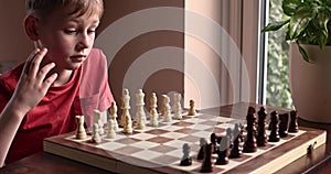 Young white child playing a game of chess on large chess board. Chess board on table in front of school boy thinking of next move