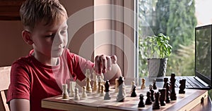 Young white child playing a game of chess on large chess board. Chess board on table in front of school boy thinking of next move