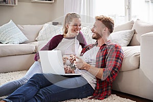 Young white couple sitting on the floor at home using laptop