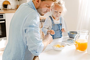 Young father and his little daughter having breakfast and using tablet computer at home