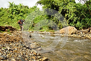 Young white man with backpack crosses the mountain river.