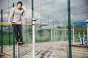 Young white man in his thirties is exercising in the street. A strong well built guy lifts the body behind the horizontal bar