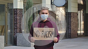 Young white man a medical mask holding carton poster with writing slogan no racism. Concept of the strike and anti