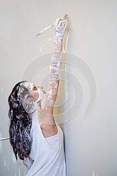 Young white painted artist woman in white underskirt with Brush and palette panting on the wall