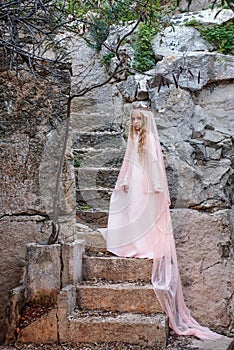 Young white pixie queen in a crown with a veil and a long dress down the stone stairs in a fabulous location