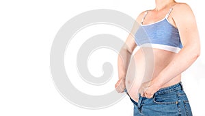 young white-skinned pregnant woman trying to fit in blue tight jeans, hands holding unfit pants