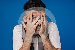 Young white unshaven man hiding his face behind hands in fear