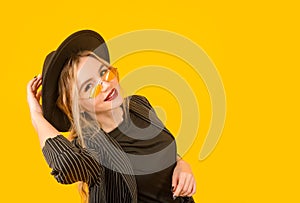 Young white woman in a black jacket and hat on a yellow background